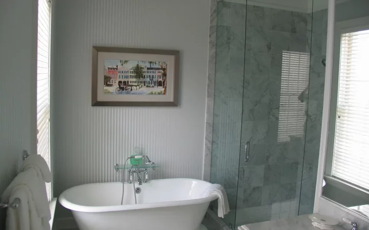 A spacious and well-lit bathroom featuring a tub that sits on a platform with tile. Next to the tub is a large walk-in shower with a glass enclosure and chrome fixtures. Light colored walls and a tile floor complete the elegant look.