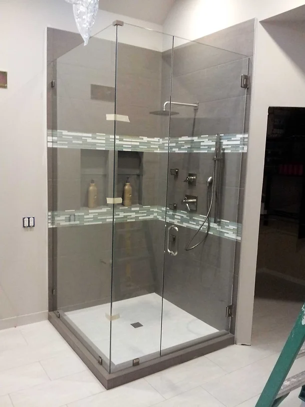 A shower stall with a transparent glass door and a chrome showerhead mounted on the wall. A shower niche on the wall for bath necessities.