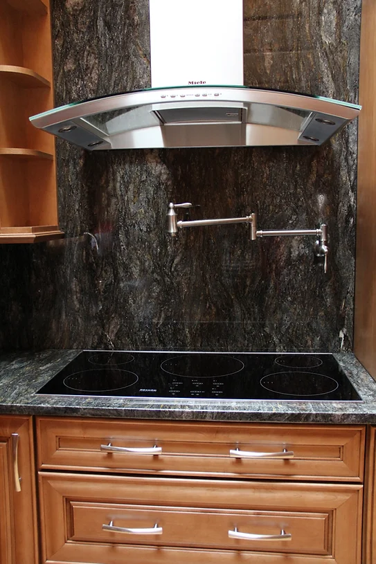 A stainless steel stovetop oven with five burners and a griddle in a modern kitchen. A stainless steel range hood is mounted above the stovetop oven.