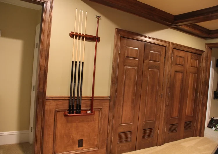 A pool cue rack mounted on a wall with wooden doors in the background.