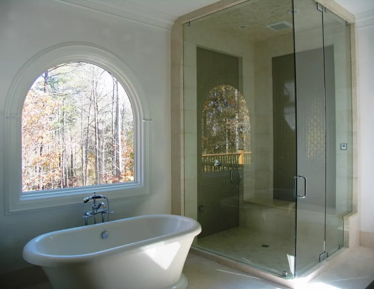 A modern bathroom with a soaking tub, a walk-in shower, and plenty of natural light from a wide window near the bathtub.