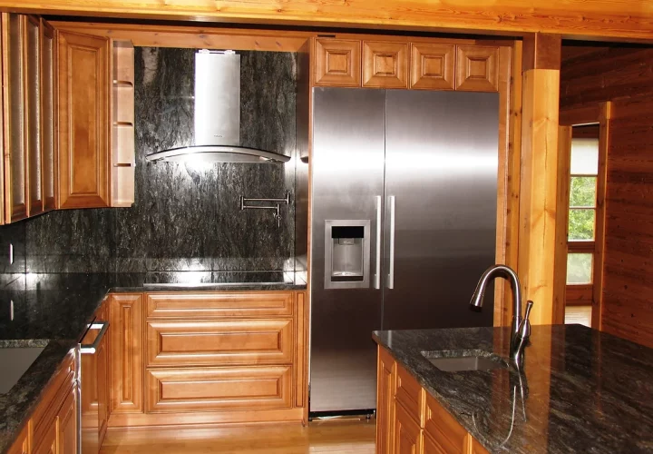 A kitchen with wooden cabinets and granite countertops. The cabinets are a light wood color, and the countertops are a dark gray. The kitchen has a modern look, with stainless steel appliances, and tiled backsplash