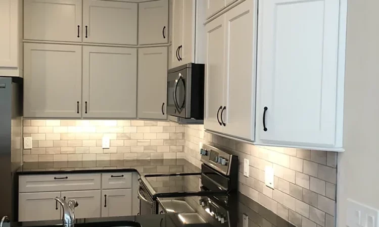 A well-lit kitchen designed for function and style. The white cabinets offer plenty of storage, while the black countertops provide a sleek and durable work surface. Stainless steel appliances and pendant lights add a touch of modern sophistication.