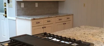 A kitchen with stove top in a granite countertop, tiled backsplash, and white cabinets